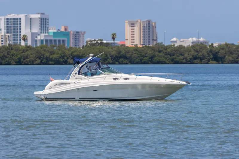 Slide: The Image of 2005 Sea Ray 340 Sundancer yacht cruising on a calm waterway with city skyline in the background. - 28