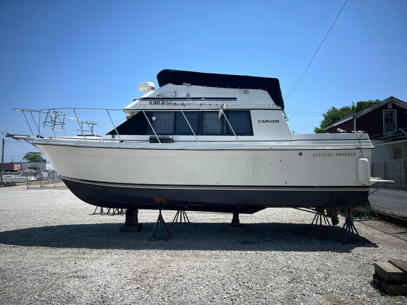 Slide: The Image of 1987 Carver Voyager boat on stands in a gravel lot, side view. - 0