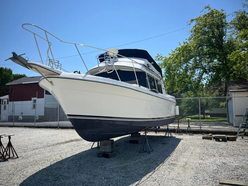 Slide: The Image of 1987 Carver Voyager boat on dry dock, white hull, blue canopy, sunny day. - 3