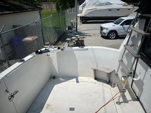 Slide: The Image of 1987 Carver Voyager boat deck with ladder, docked near parked vehicles and fenced area. - 8