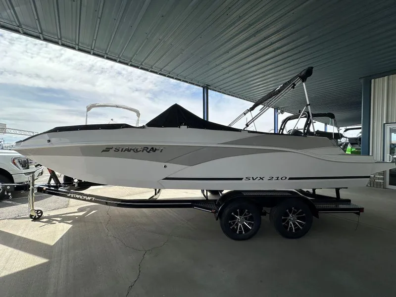 Slide: The Image of 2024 Starcraft SVX 210 OB DC boat on a trailer under a metal canopy. - 1