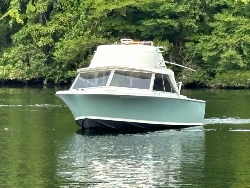 Slide: The Image of 1966 Bertram 25 boat cruising on a serene lake with lush green trees. - 0