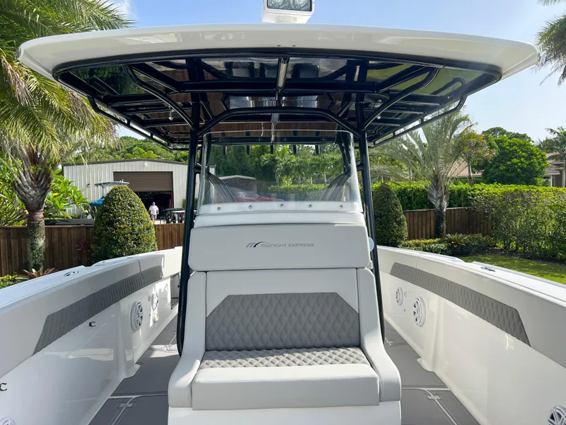 Slide: The Image of 2014 Midnight Express 37 Open boat with seating and canopy, docked in a lush, green area. - 23
