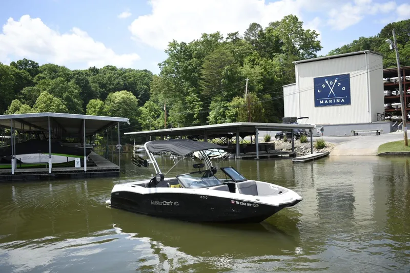 Slide: The Image of 2022 MasterCraft NXT22 boat docked at a marina with lush green trees in the background. - 26