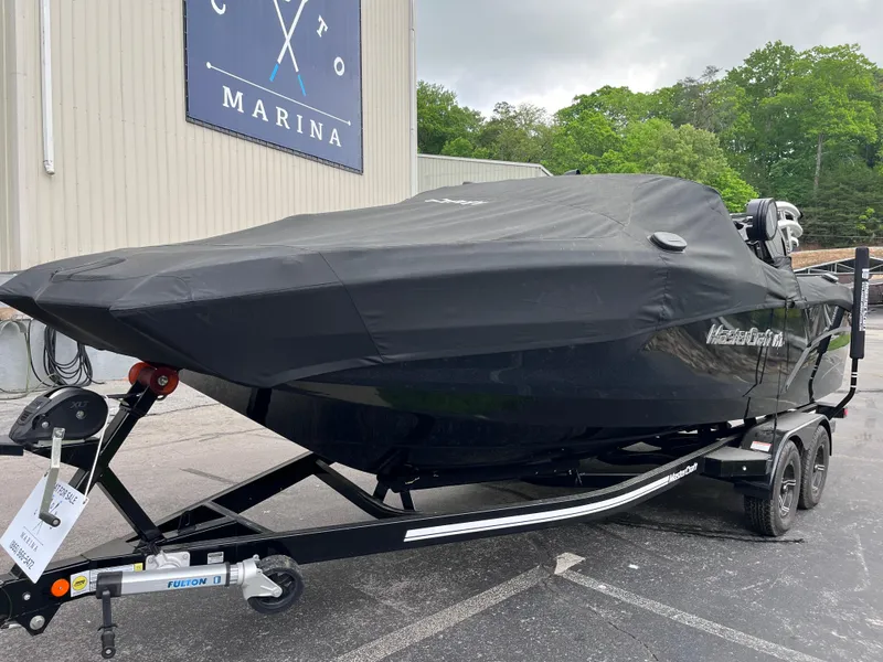 Slide: The Image of 2022 MasterCraft NXT22 boat with cover on trailer, parked near marina building. - 30