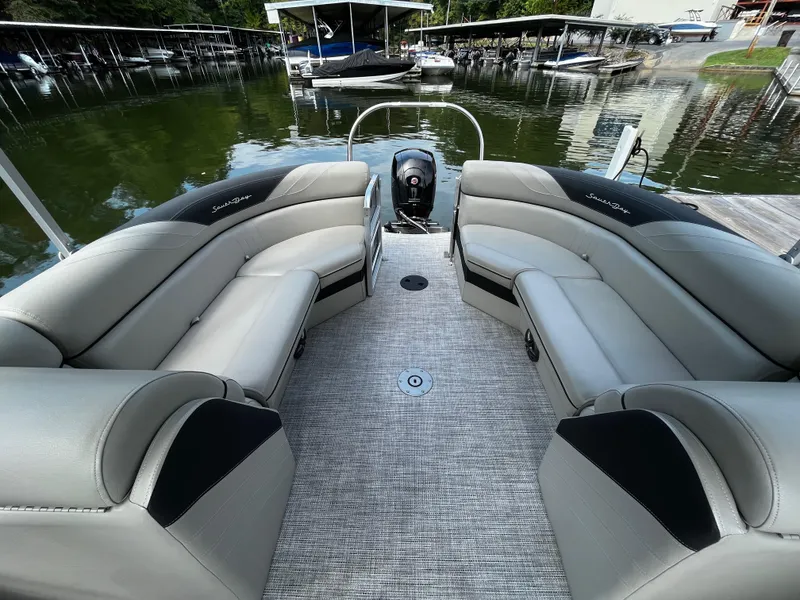 Slide: The Image of 2022 South Bay 224 RS LE pontoon boat interior with plush seating at a marina. - 14
