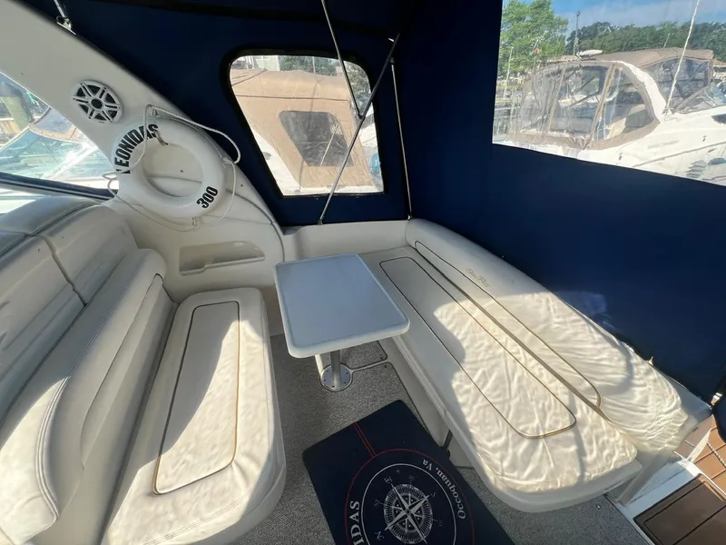 Slide: The Image of 2003 Sea Ray 300 Sundancer interior with cushioned seating and table, featuring a blue canopy. - 5