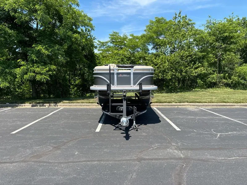 Slide: The Image of 2024 Sun Tracker Party Barge 20 DLX parked in a lot, surrounded by greenery. - 5