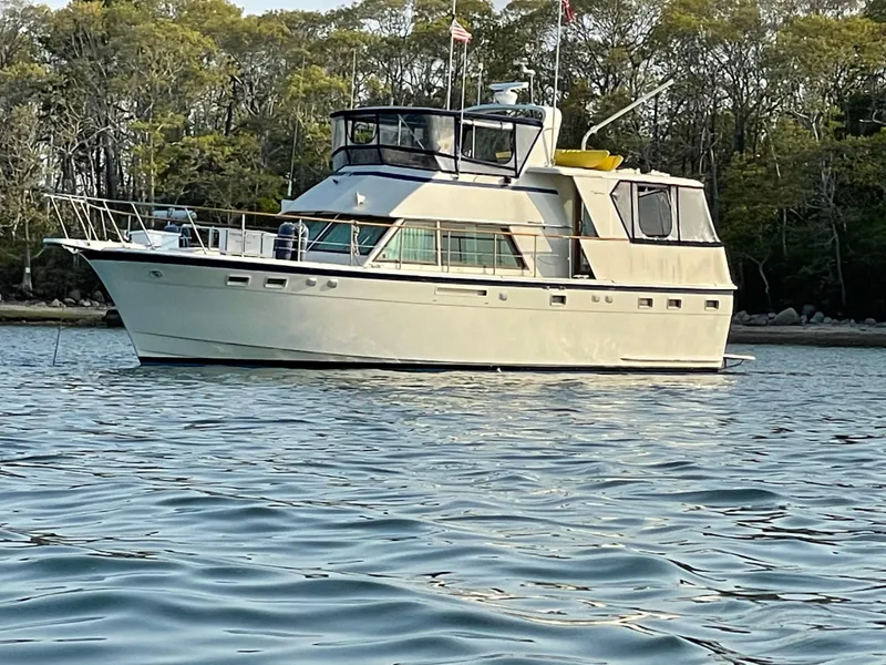 Slide: The Image of 1981 Hatteras 48 Motor Yacht anchored on calm water with forested background. - 2