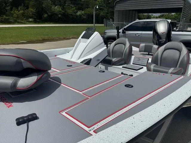 Slide: The Image of 2024 Xpress Boats H18 fishing boat with gray and red interior, docked near a vehicle. - 11