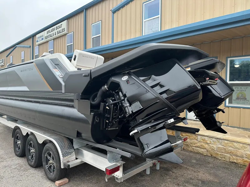 Slide: The Image of 2024 Manitou Explore Navigator Dual Engine Rotax boat on a trailer outside a sales building. - 2