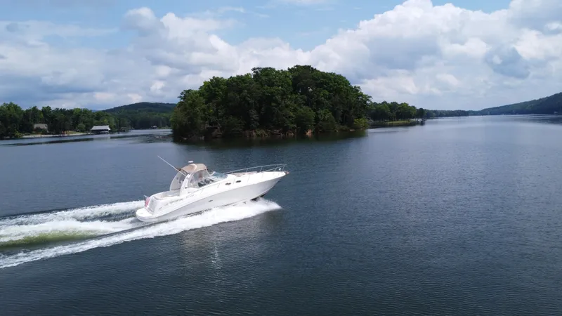 The Image of Sea Ray 340 Sundancer 2003 cruising on a serene lake with lush island backdrop. - 1