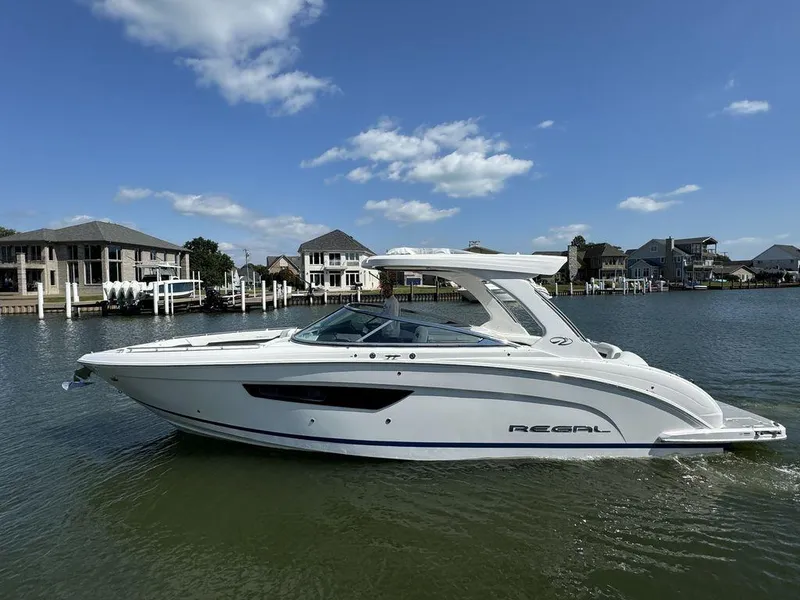 Slide: The Image of 2025 Regal 3300 boat cruising on a sunny day near waterfront homes. - 0