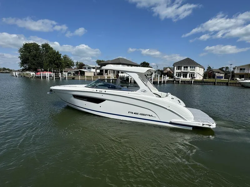 Slide: The Image of 2025 Regal 3300 boat cruising on a scenic waterway with houses in the background. - 1