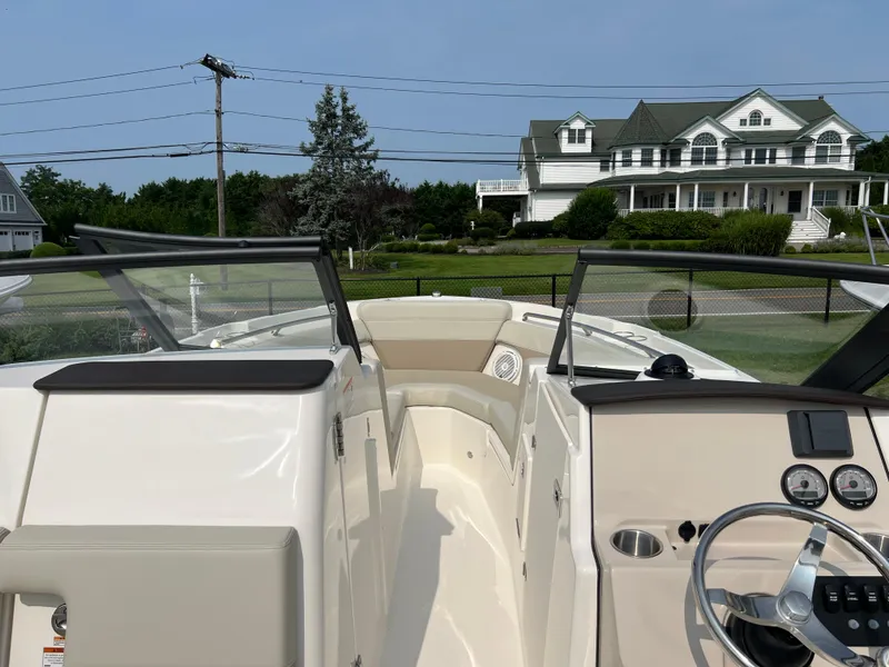 Slide: The Image of 2025 Boston Whaler 210 Vantage boat interior with steering wheel, gauges, and seating, near a house. - 13