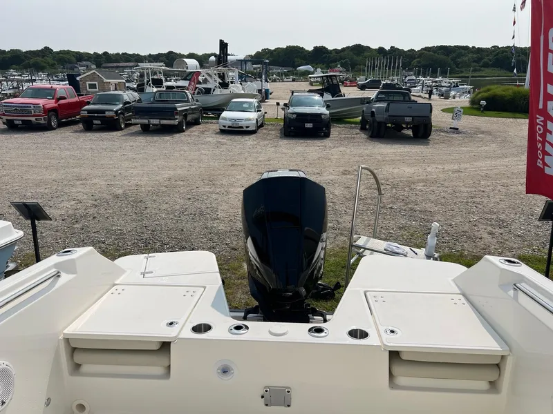 Slide: The Image of 2025 Boston Whaler 210 Vantage boat at marina with parked vehicles in background. - 3