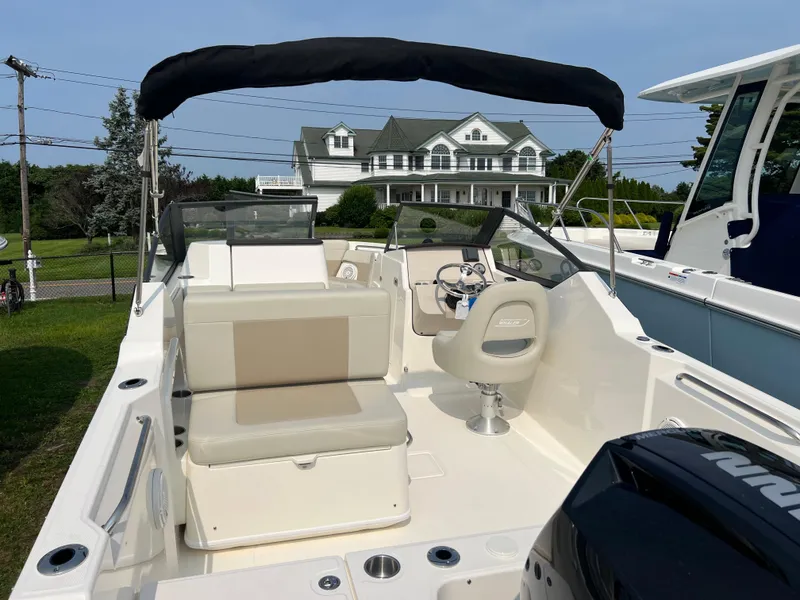 Slide: The Image of 2025 Boston Whaler 210 Vantage boat with seating and canopy, parked near a house. - 4