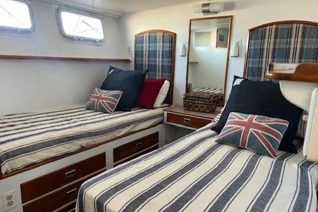 Slide: The Image of 1970 Huckins Offshore cabin with twin beds, nautical decor, and Union Jack pillows. - 13