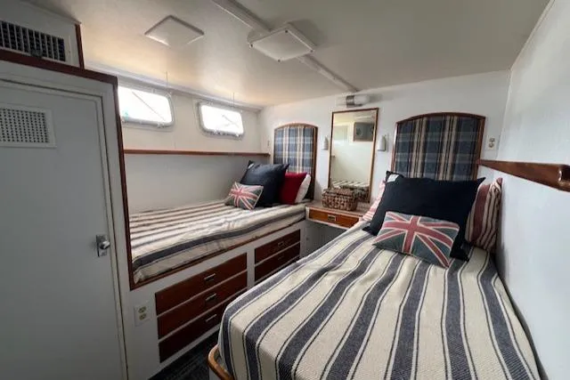 Slide: The Image of 1970 Huckins Offshore cabin with twin beds, striped bedding, and Union Jack pillows. - 23