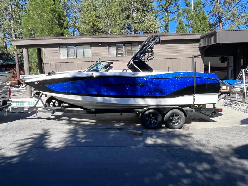 Slide: The Image of 2024 MasterCraft X24 boat on a trailer in front of a house with trees. - 1