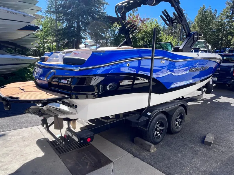 Slide: The Image of 2024 MasterCraft X24 boat on trailer, blue and white exterior, parked outdoors. - 2