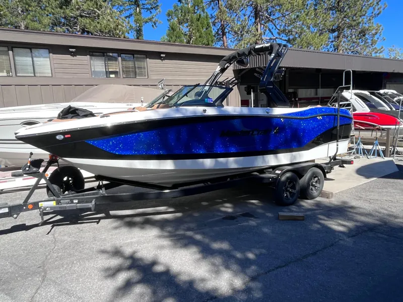 Slide: The Image of 2024 MasterCraft X24 boat on a trailer, blue and white, parked outdoors. - 4