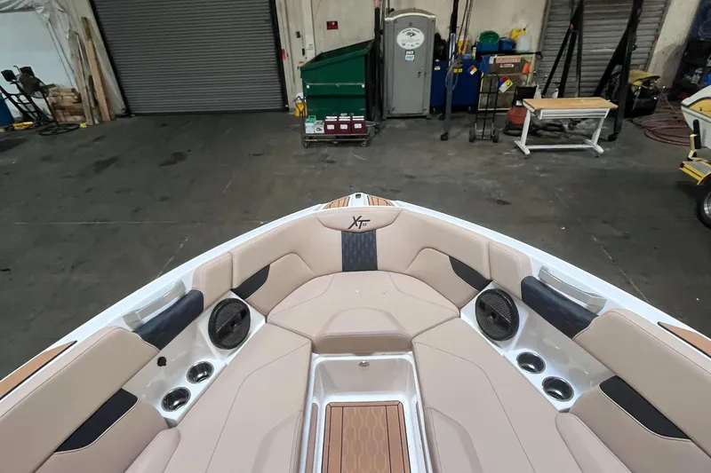 Slide: The Image of 2024 MasterCraft XT23 boat interior with beige seating and speakers in a warehouse setting. - 16