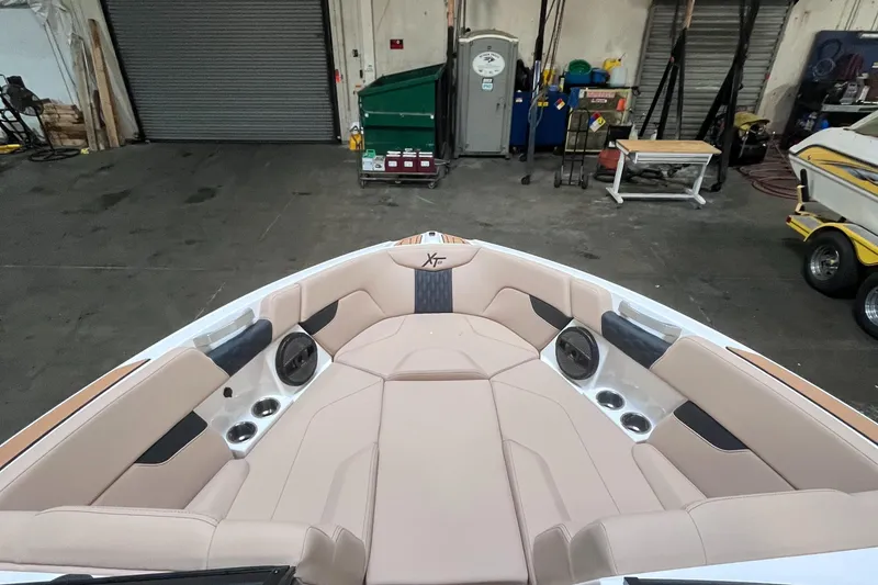 Slide: The Image of 2024 MasterCraft XT23 boat interior with beige seating and cup holders in a garage. - 17