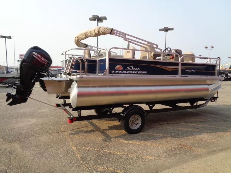 Slide: The Image of 2024 Sun Tracker Bass Buggy 18 DLX pontoon boat on trailer in parking lot. - 2