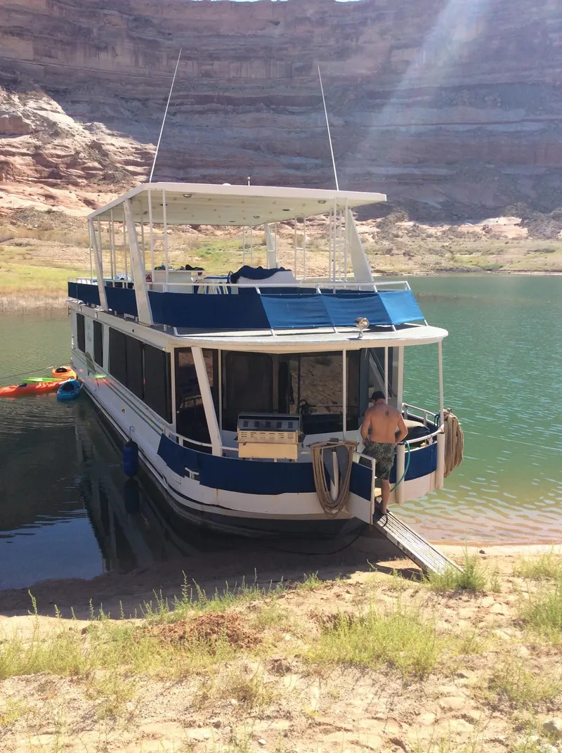 Slide: The Image of 2001 Skipperliner Houseboat docked on a serene lake with rocky cliffs in the background. - 3