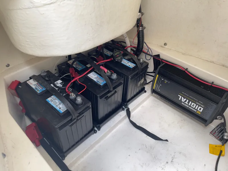 Slide: The Image of 2019 Tidewater 2410 Bay Max boat battery compartment with three batteries and a charger. - 29