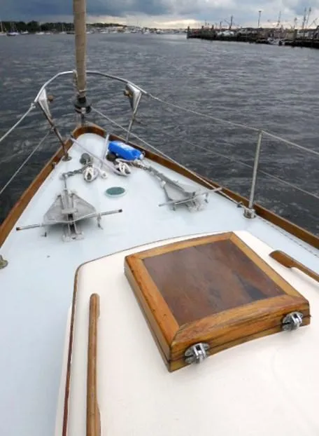 Slide: The Image of Bow of 1961 Rhodes Swiftsure sailboat on water, featuring wooden hatch and anchor. - 48