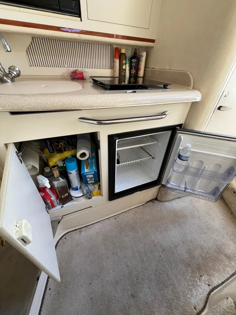 Slide: The Image of Compact kitchenette in a 2001 Sea Ray 270 Sundancer with open cabinets and mini-fridge. - 33