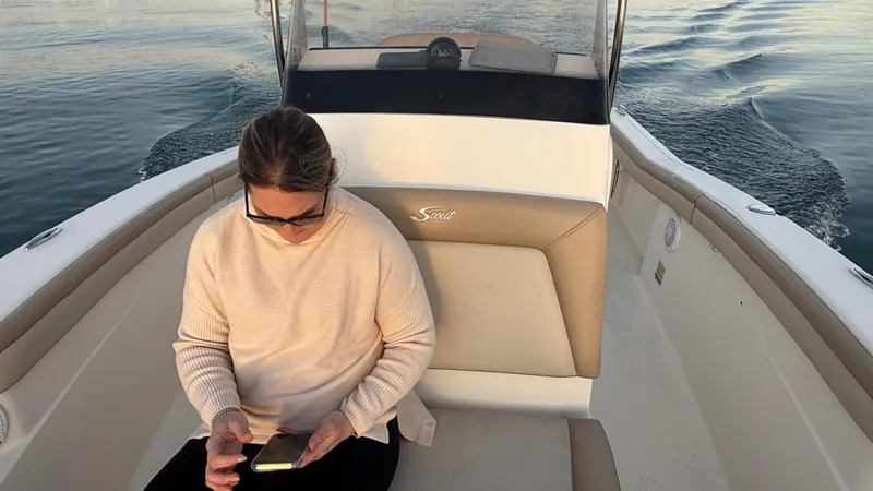 Slide: The Image of Woman on 2021 Scout 215 XSF boat using phone, calm waters in background. - 42