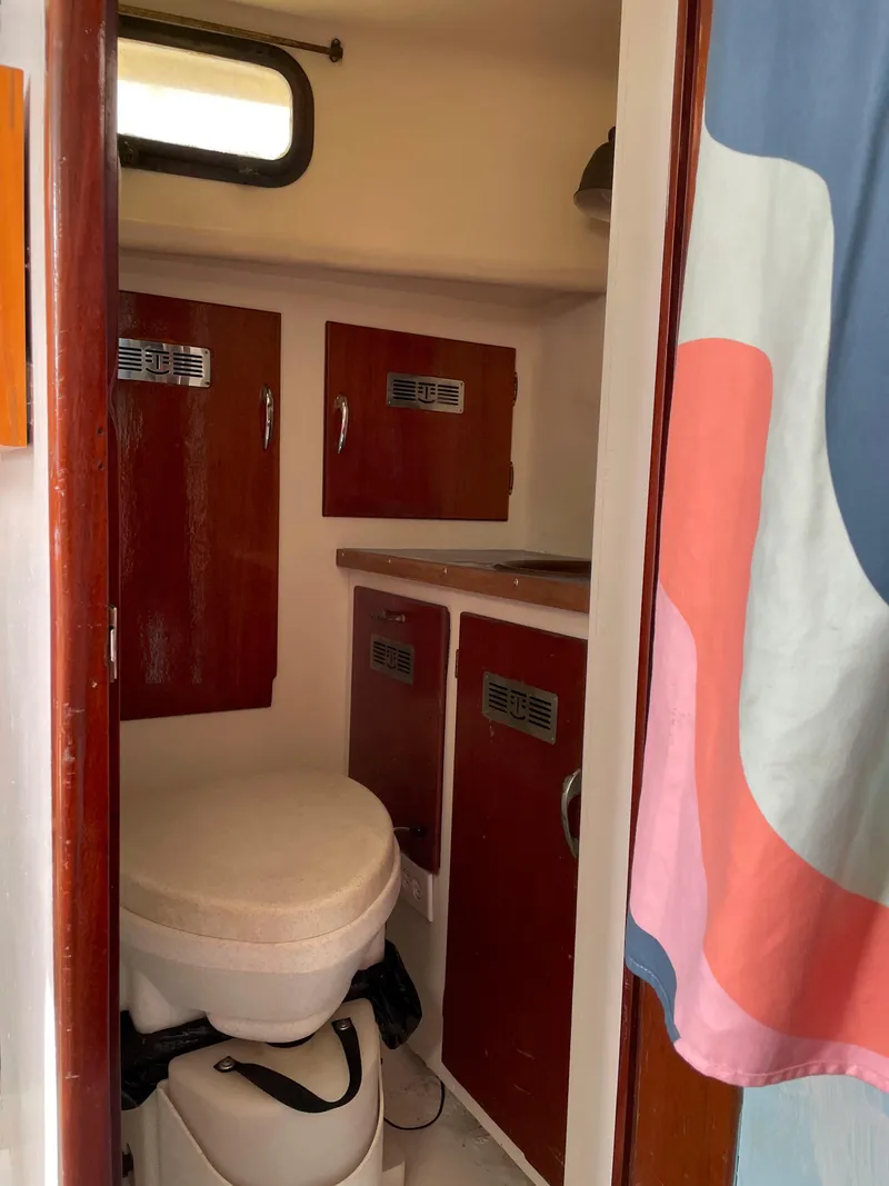 Slide: The Image of Interior of 1960 Rhodes Bounty II sailboat bathroom with wooden cabinets and colorful curtain. - 12