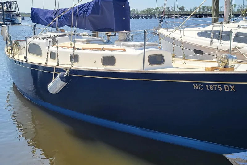 Slide: The Image of 1960 Rhodes Bounty II sailboat docked, featuring a sleek blue hull and covered deck. - 23