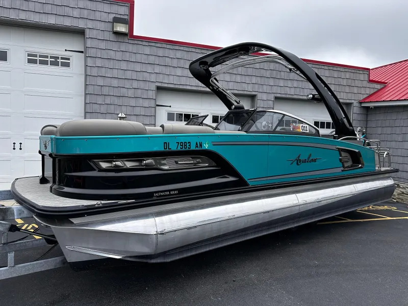 Slide: The Image of 2021 Avalon Excalibur 2585 Windshield Elite Tri Toon boat, teal and black, parked outdoors. - 1