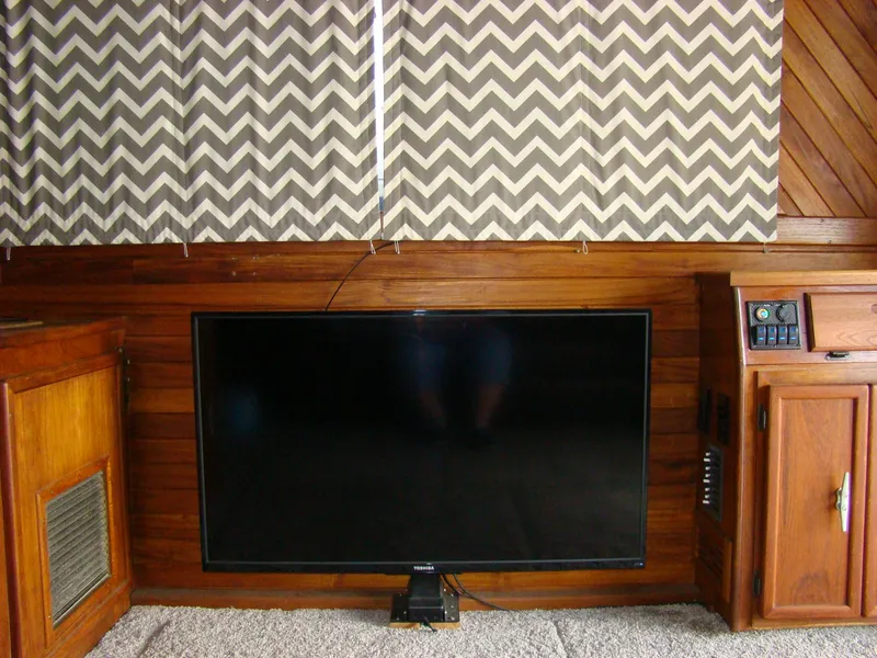 Slide: The Image of Flat-screen TV in a 1985 Jersey Dawn 40 boat interior with wood paneling and chevron curtains. - 44
