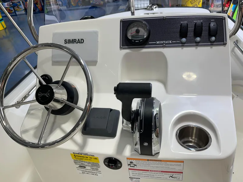Slide: The Image of 2024 Boston Whaler 150 Montauk boat console with steering wheel and Simrad electronics. - 2