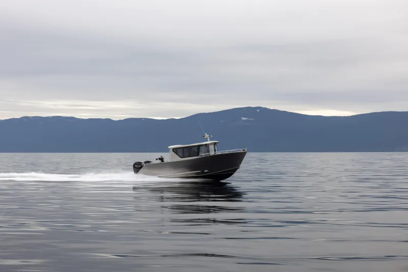 Slide: The Image of 2025 Jasper Marine Defender 22 boat cruising on calm waters with mountainous backdrop. - 22