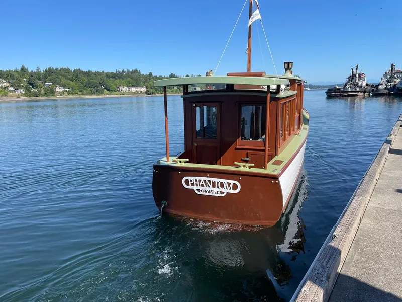 Slide: The Image of 1931 Jensen Cruiser boat on calm water near a dock, under clear blue sky. - 32