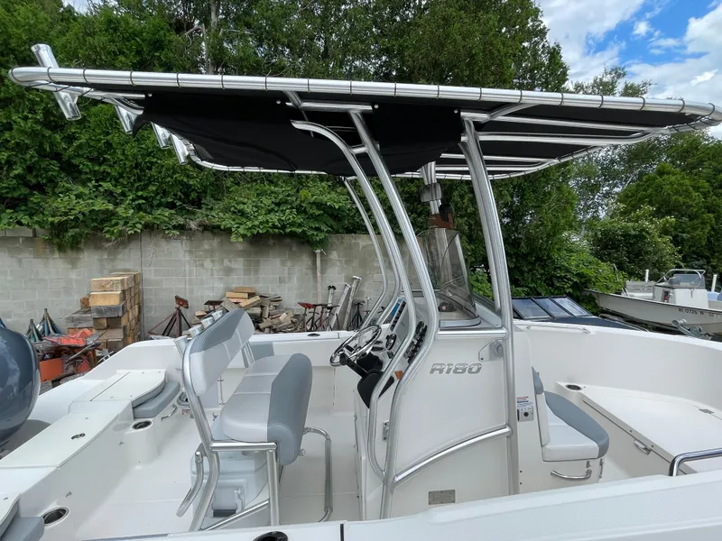 Slide: The Image of 2021 Robalo R180 Center Console boat with T-top, white seating, and lush green backdrop. - 10