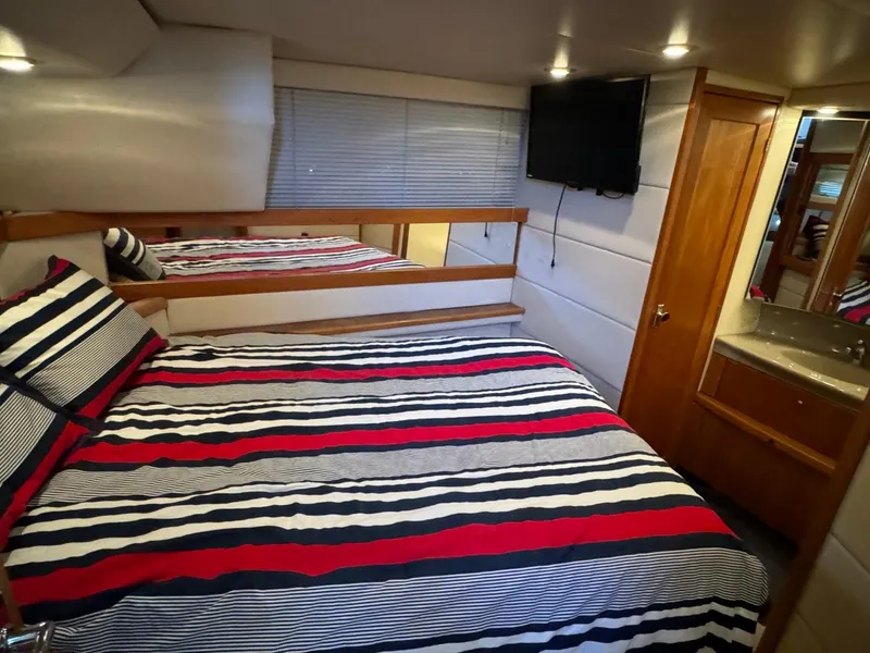Slide: The Image of 1999 Bayliner 4087 Aft Cabin Motor Yacht bedroom with striped bedding and wall-mounted TV. - 23