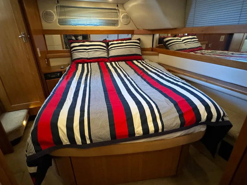 Slide: The Image of 1999 Bayliner 4087 Aft Cabin Motor Yacht bedroom with striped bedding and wood accents. - 25