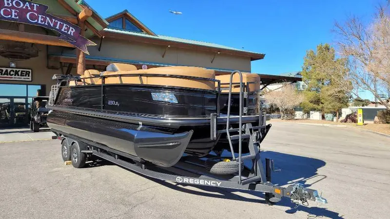 Slide: The Image of 2024 Regency 230 LE3 Sport pontoon boat on trailer outside service center. - 2