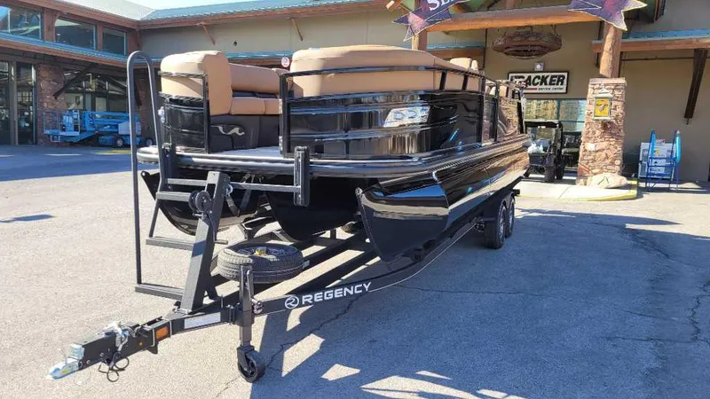 Slide: The Image of 2024 Regency 230 LE3 Sport pontoon boat on trailer, parked outside a building. - 4