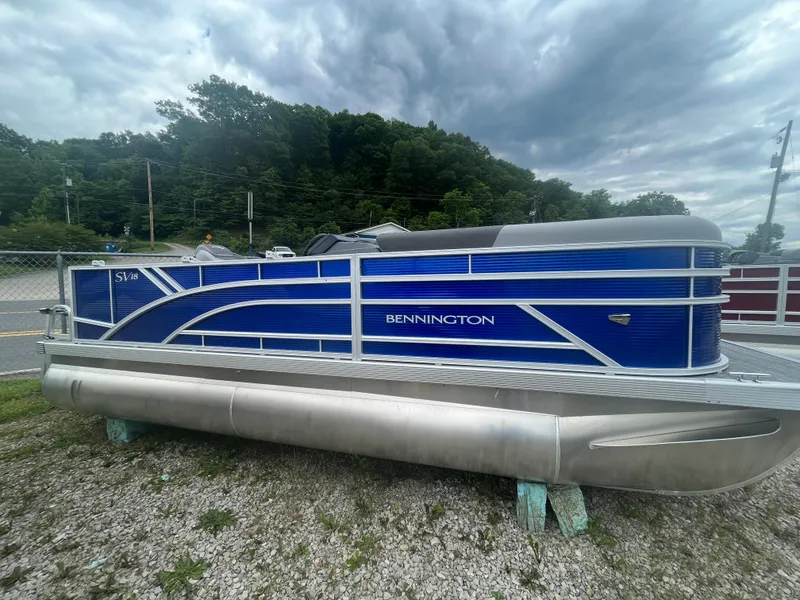Slide: The Image of 2024 Bennington 188 SVL pontoon boat with blue exterior on gravel lot. - 1