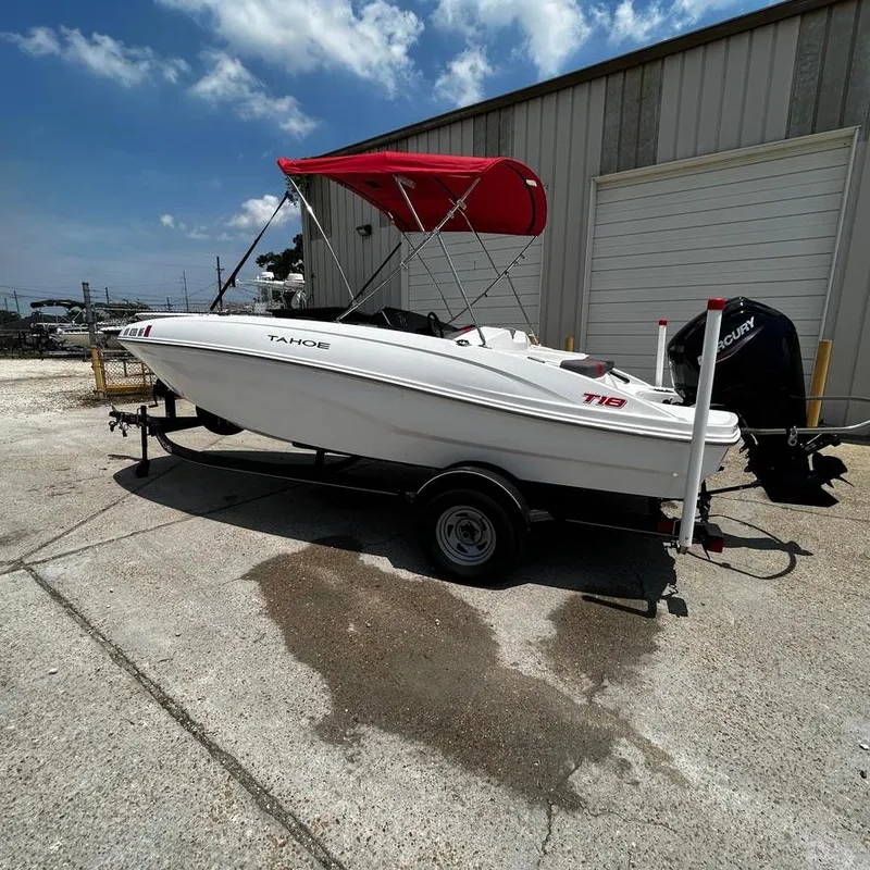 Slide: The Image of 2022 Tahoe T18 boat with red canopy on trailer, parked outside a warehouse. - 11