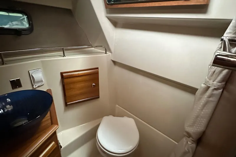 Slide: The Image of 2021 Ranger Tugs R-27 boat bathroom with toilet, sink, and shower curtain. - 12