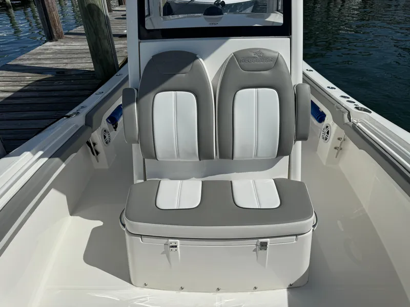 Slide: The Image of 2024 Regulator 23 boat seating with gray and white upholstery, dockside view. - 49